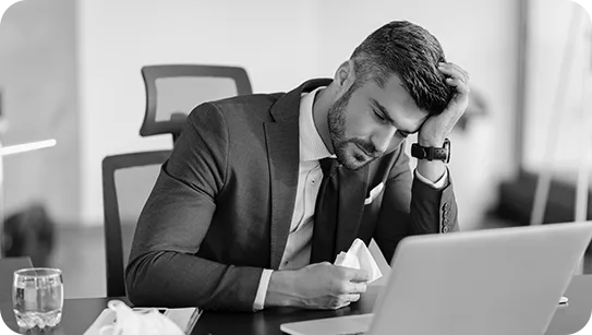 Black and white photo of a stressed man in a suit with his head in his hand at a laptop